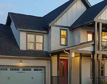 Front view of a home with white vinyl siding by Mastic, and with the lights from the windows turned on as nighttime sets in