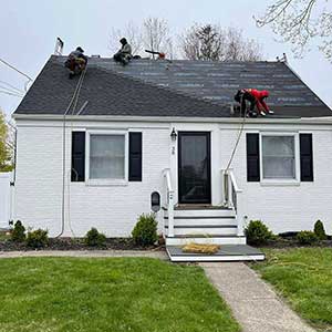 Front view of South County Exteriors workers installing new dark gray shingles on a small residential home